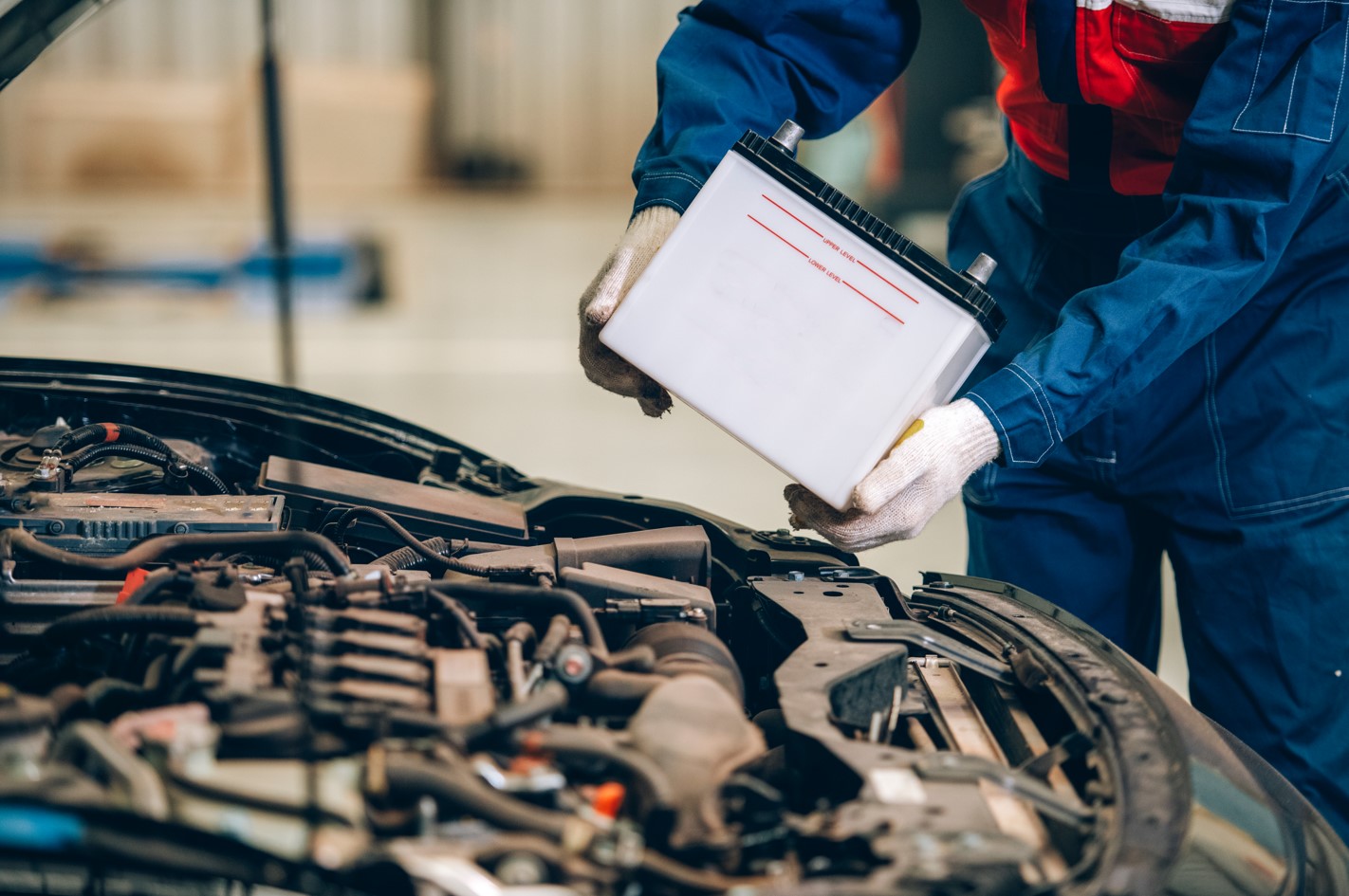 A photo of a mechanic putting a battery in a car.