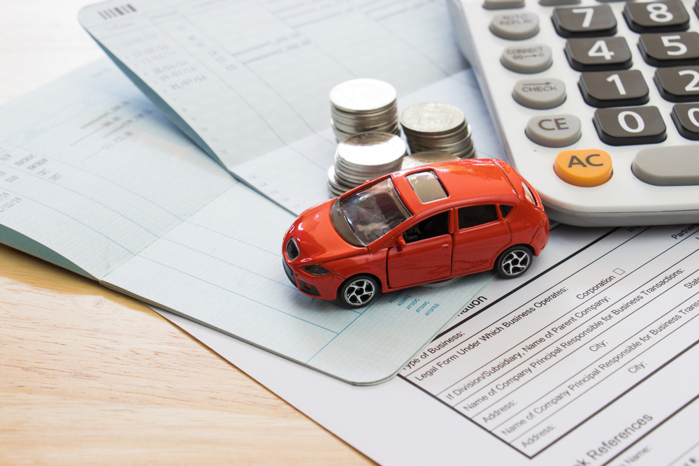 A photo of a toy car sitting on a desk with paperwork, coins, and a calculator.