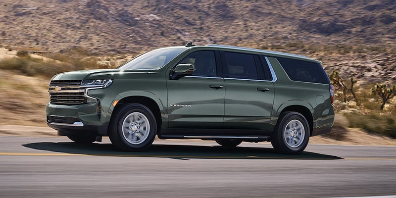A photo of a green 2024 Chevy Suburban driving down a desert highway
