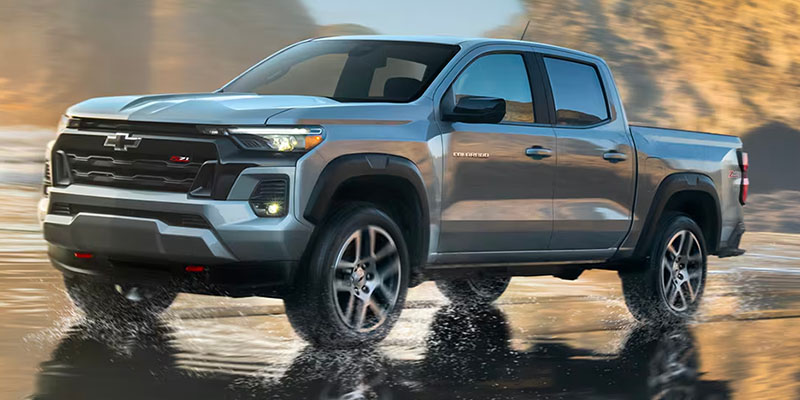 A photo of a grey 2025 Chevy Colorado driving on a wet street.
