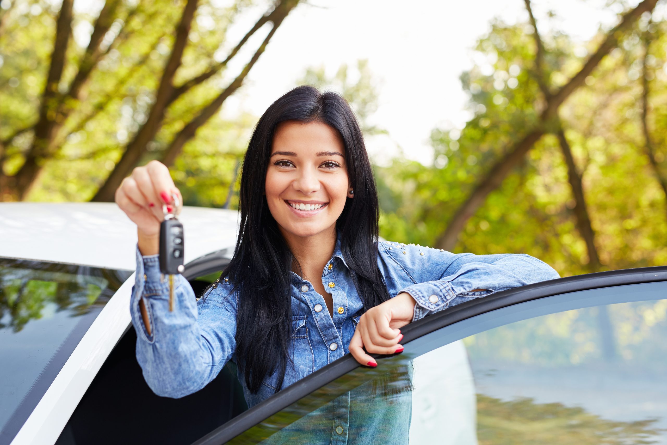 A woman standing at a car and holding car keys.