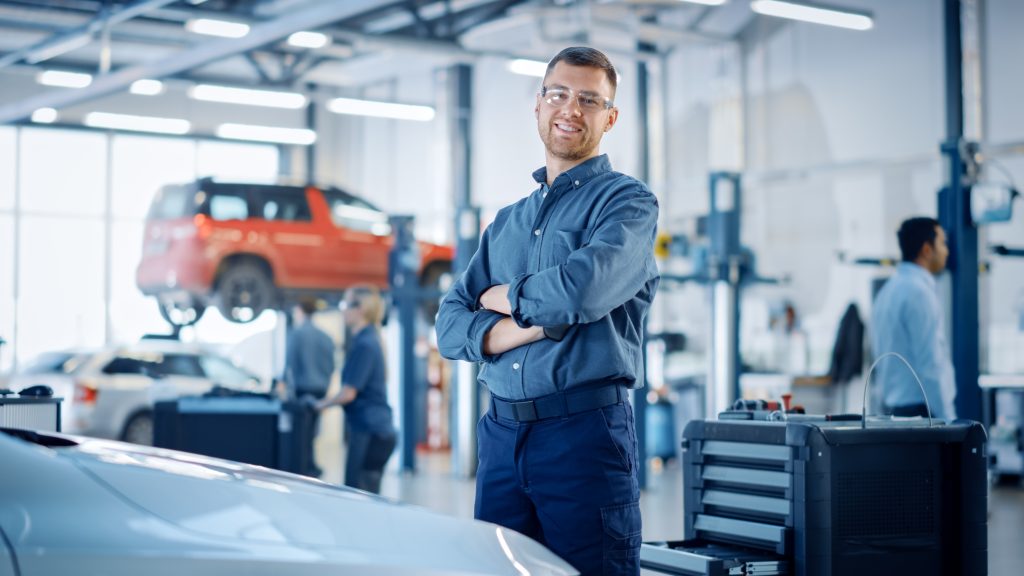 A mechanic smiling and posing in a car repair shop.
